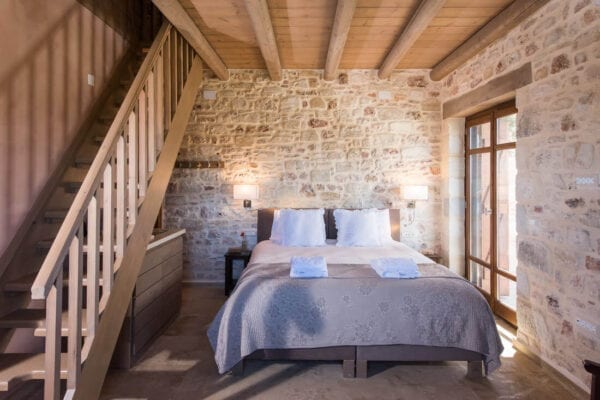A bedroom with stone walls and a wooden staircase.