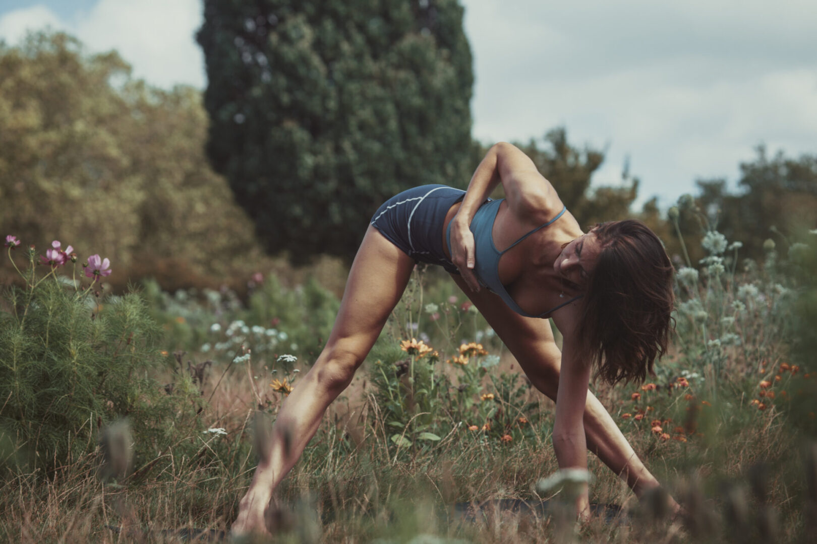 A woman in shorts and top doing yoga on grass.