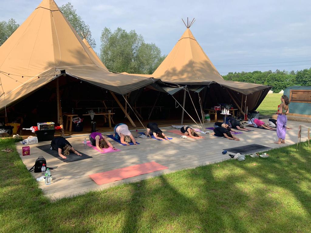 A group of people doing yoga in front of tents.