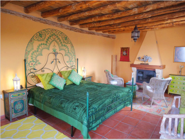 A bed room with a green bedspread and a fireplace